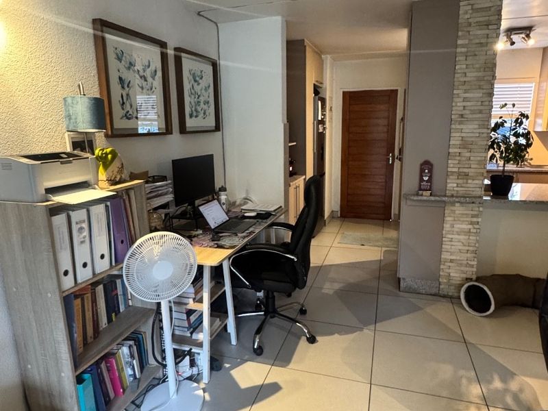 Open plan living area featuring large floor tiles and a decorative stone-clad pillar, providing a functional layout with access to adjacent rooms.