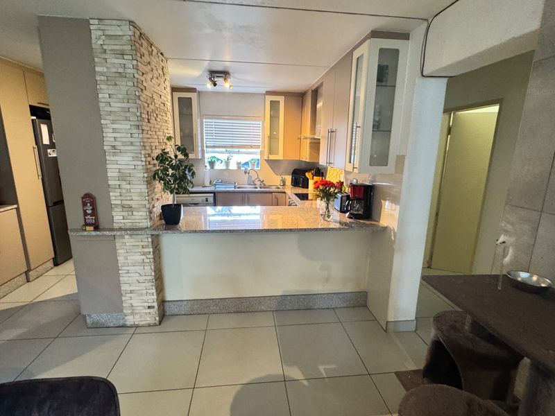 A functional kitchen featuring granite countertops, stone veneer accents, and ample cabinetry, providing a practical workspace with a breakfast bar overlooking the living area.