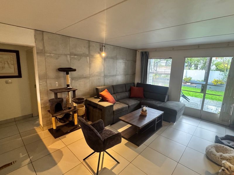 A bright living room featuring large format floor tiles, a modern concrete-look feature wall, and direct access to the rear patio through sliding glass doors.
