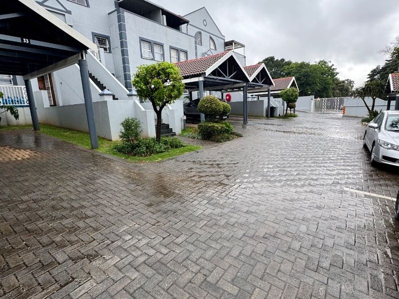 Exterior view of a townhouse complex featuring paved driveways, covered parking bays, and multi-level residential units under a cloudy sky.