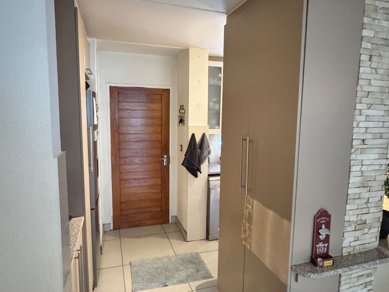 A functional kitchen area featuring tiled flooring, built-in cabinetry, and a decorative stone-cladding feature wall, leading to a solid wood interior door.