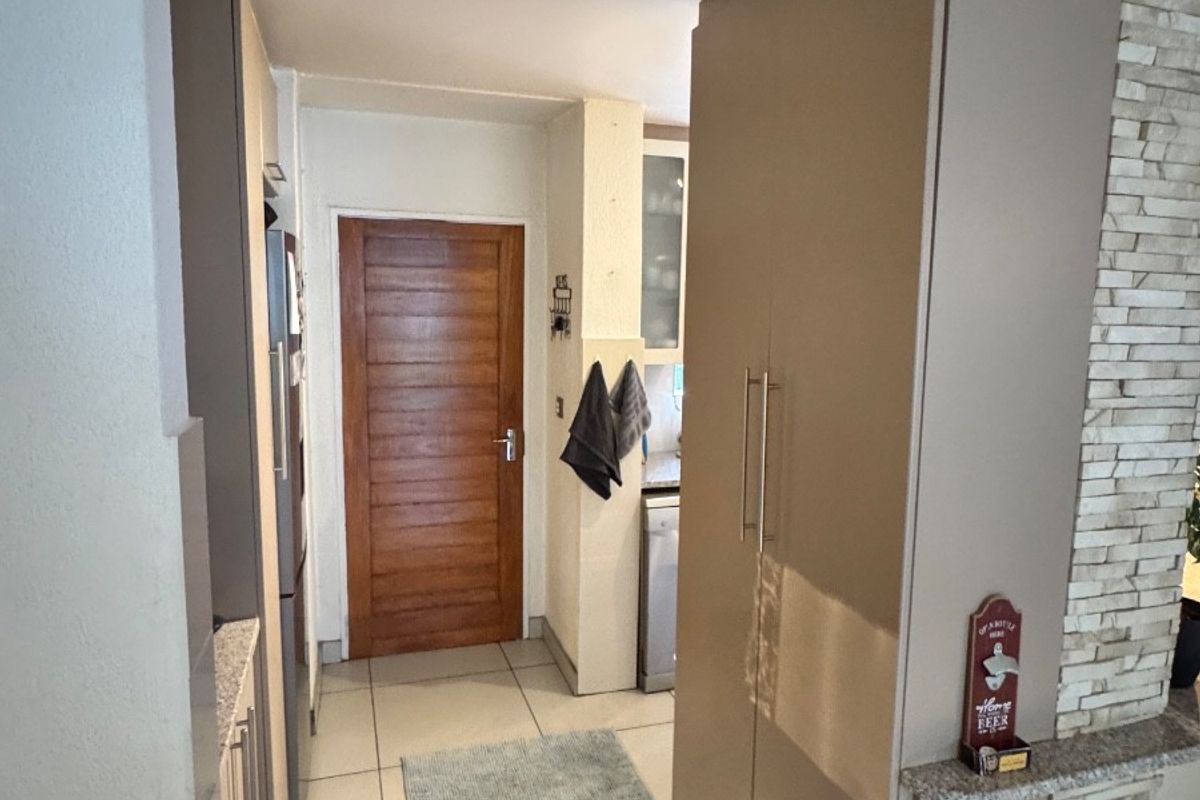 A functional kitchen area featuring tiled flooring, built-in cabinetry, and a decorative stone-cladding feature wall, leading to a solid wood interior door.