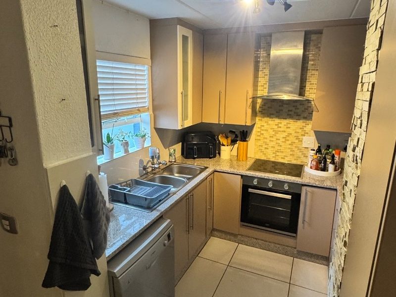 Compact kitchen featuring built-in cabinetry, granite countertops, stainless steel appliances, and a mosaic tile backsplash with tiled flooring.