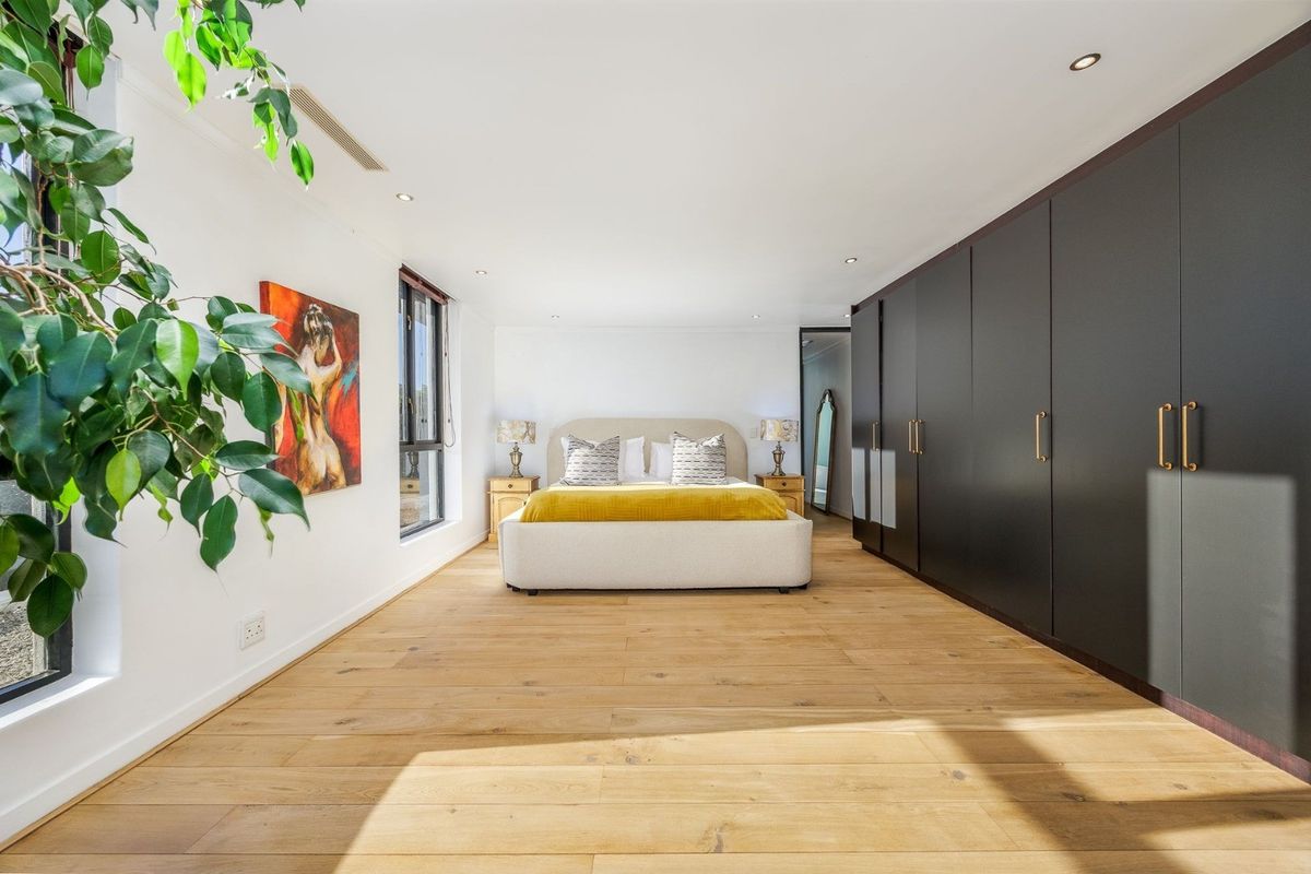 Spacious bedroom featuring light timber flooring, extensive dark built-in cabinetry, and recessed downlighting.