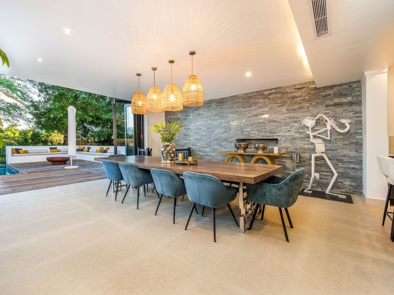Spacious open-plan dining area featuring a striking stone feature wall, recessed lighting, and seamless indoor-outdoor flow through large stacking glass doors to the patio.