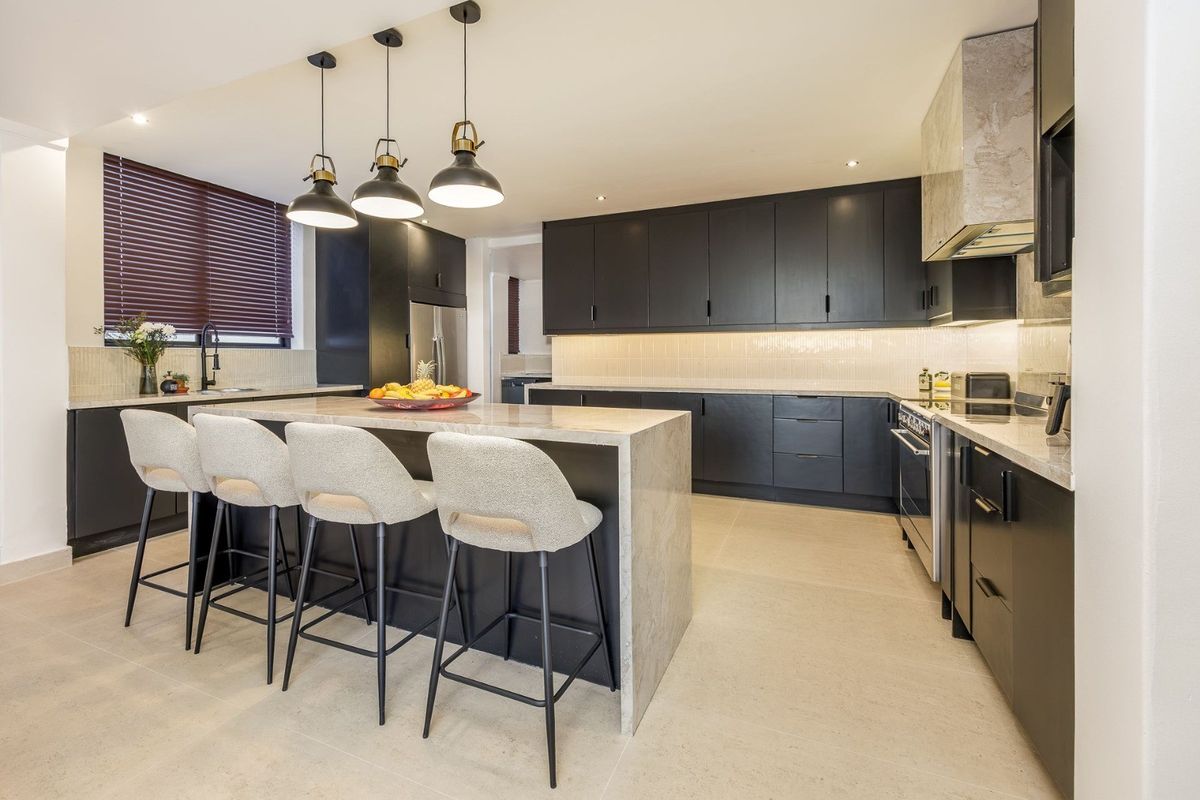 Modern kitchen featuring dark cabinetry, a large stone-topped island with breakfast bar seating, integrated appliances, and stylish pendant lighting.