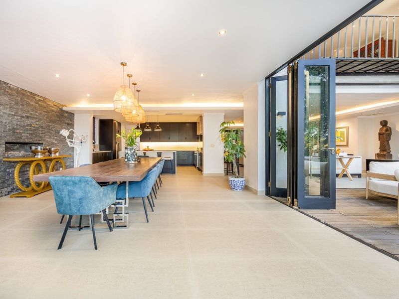 Spacious open-plan living and dining area featuring a stone feature wall, modern kitchen cabinetry, and seamless indoor-outdoor flow through large bi-fold doors.