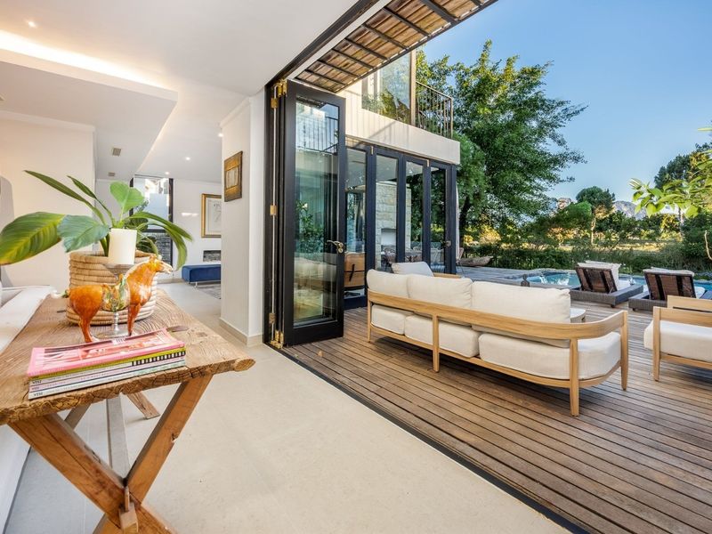 A seamless indoor-outdoor living space featuring timber decking, bi-fold doors, and a direct view of the swimming pool and garden.