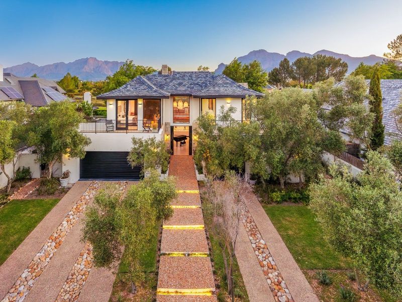 A stunning double-story residence featuring a slate roof, double garage, and a beautifully landscaped driveway with integrated lighting, set against a mountain backdrop.