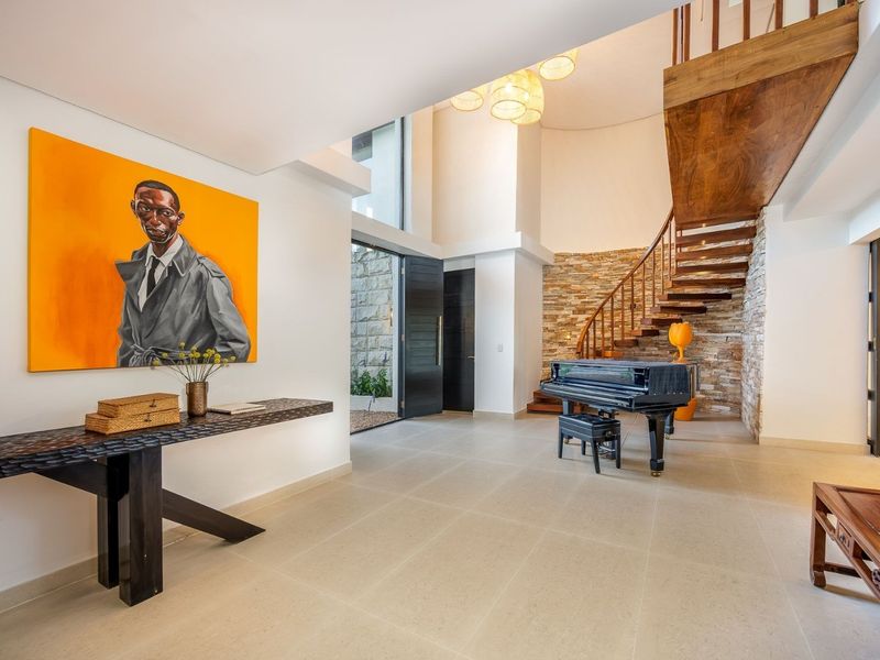Spacious double-volume entrance hall featuring a striking stone feature wall, elegant wooden staircase, and large-format floor tiles.