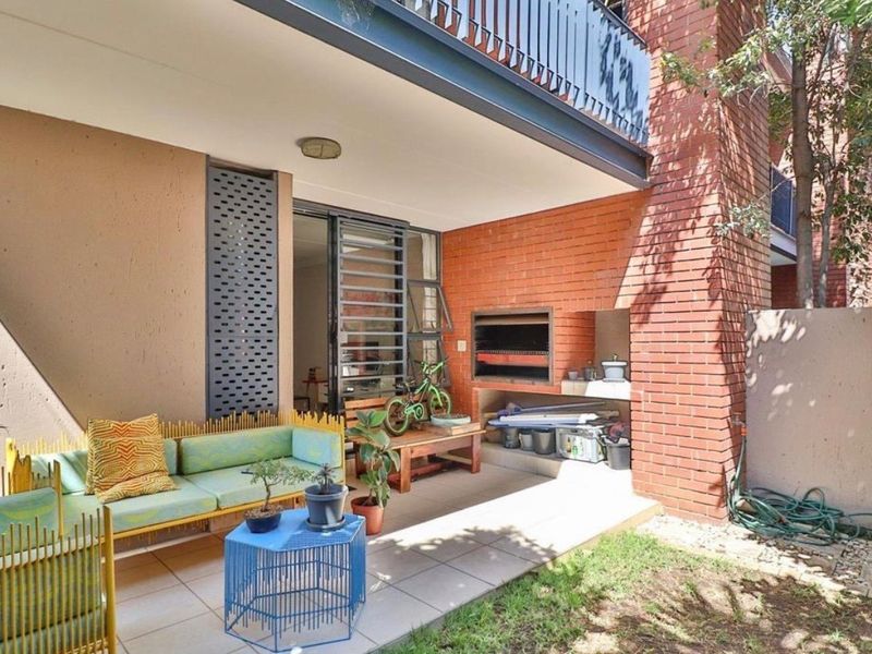 Covered patio area featuring a built-in brick braai, tiled flooring, and direct access to the interior through sliding doors.