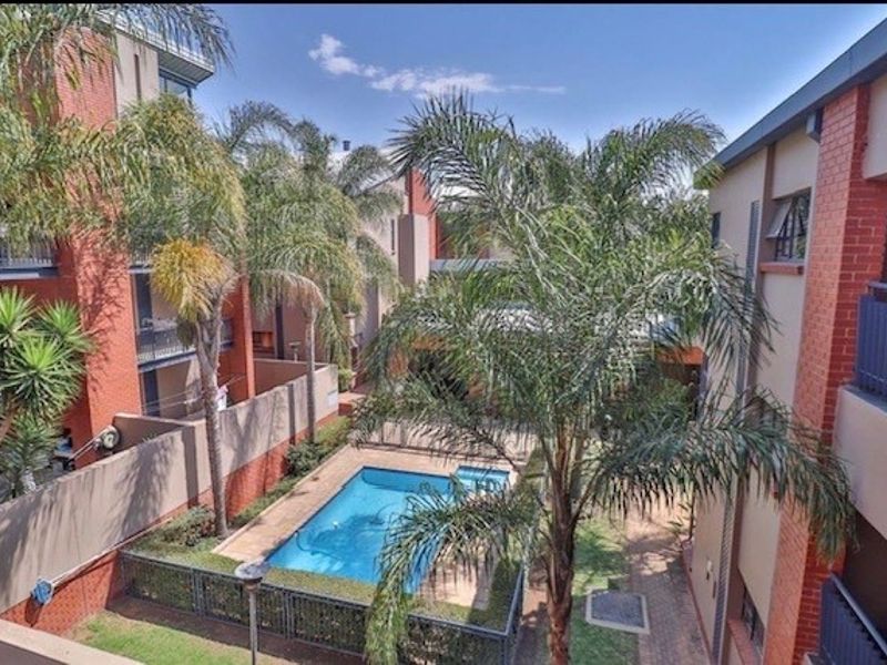 Elevated view of a communal apartment complex courtyard featuring a swimming pool, landscaped garden areas, and brick building facades with balconies.