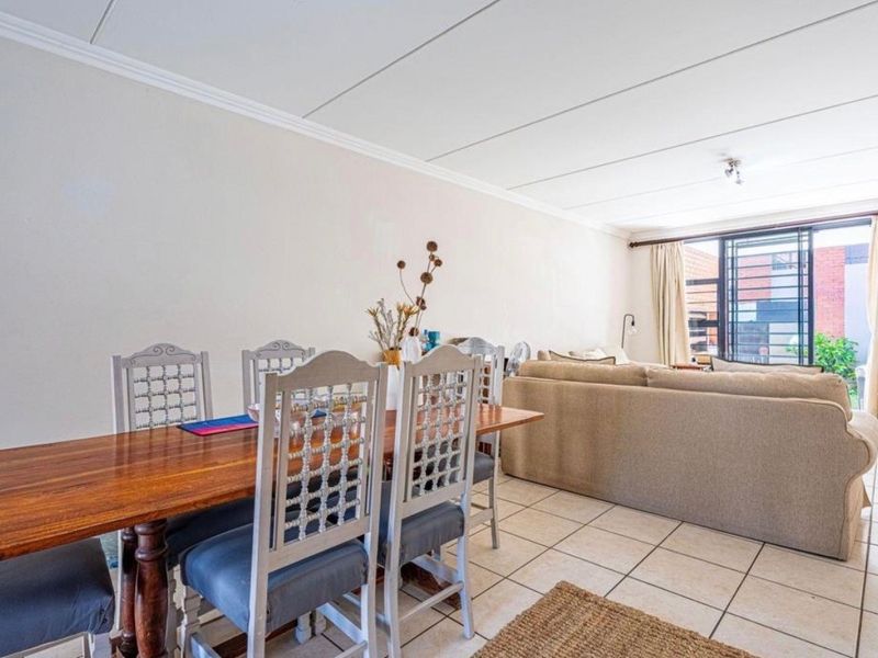 An open-plan living and dining area featuring tiled flooring, neutral walls, and a sliding door leading to an outdoor space with security bars.