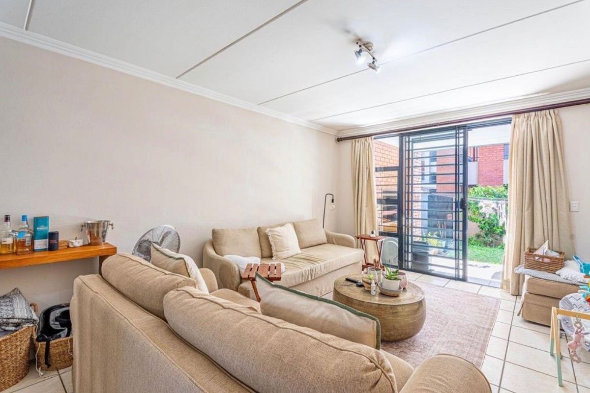 A bright living room featuring tiled floors and a sliding glass door with security gate, providing direct access to the outdoor area.