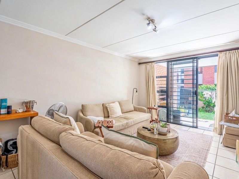 A bright living room featuring tiled floors and a sliding glass door with security gate, providing direct access to the outdoor area.