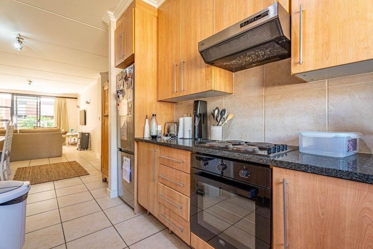 A functional kitchen featuring light wood cabinetry, granite countertops, a built-in oven, and an electric hob, flowing into an open-plan living area.