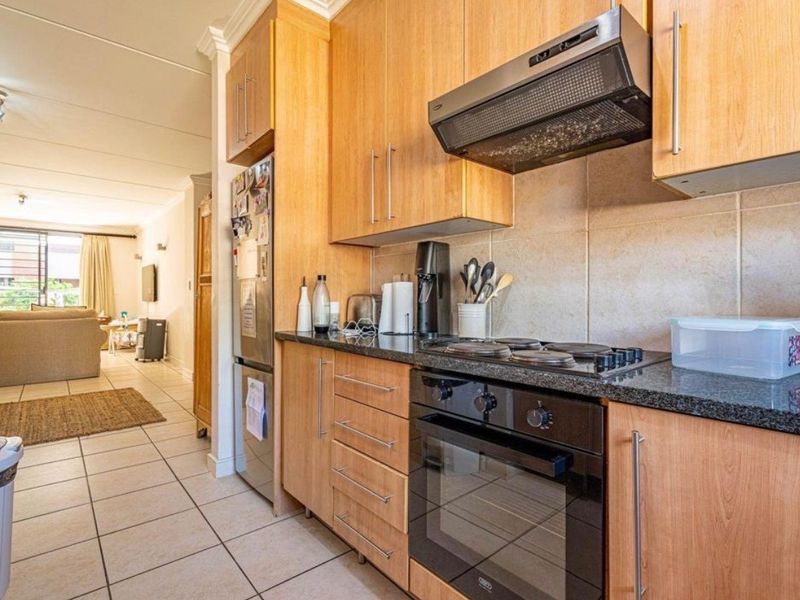 A functional kitchen featuring light wood cabinetry, granite countertops, a built-in oven, and an electric hob, flowing into an open-plan living area.