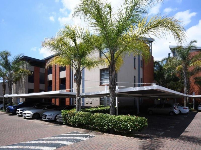 Exterior view of the apartment complex featuring covered parking bays, paved driveway, and established landscaping.