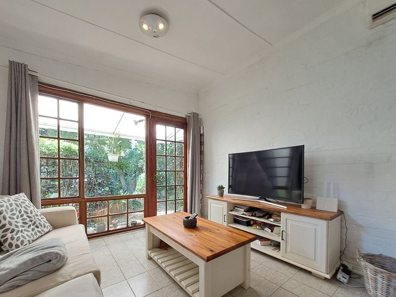 A cozy living room featuring tiled floors, white textured walls, and large timber-framed glass doors providing direct access to the garden.