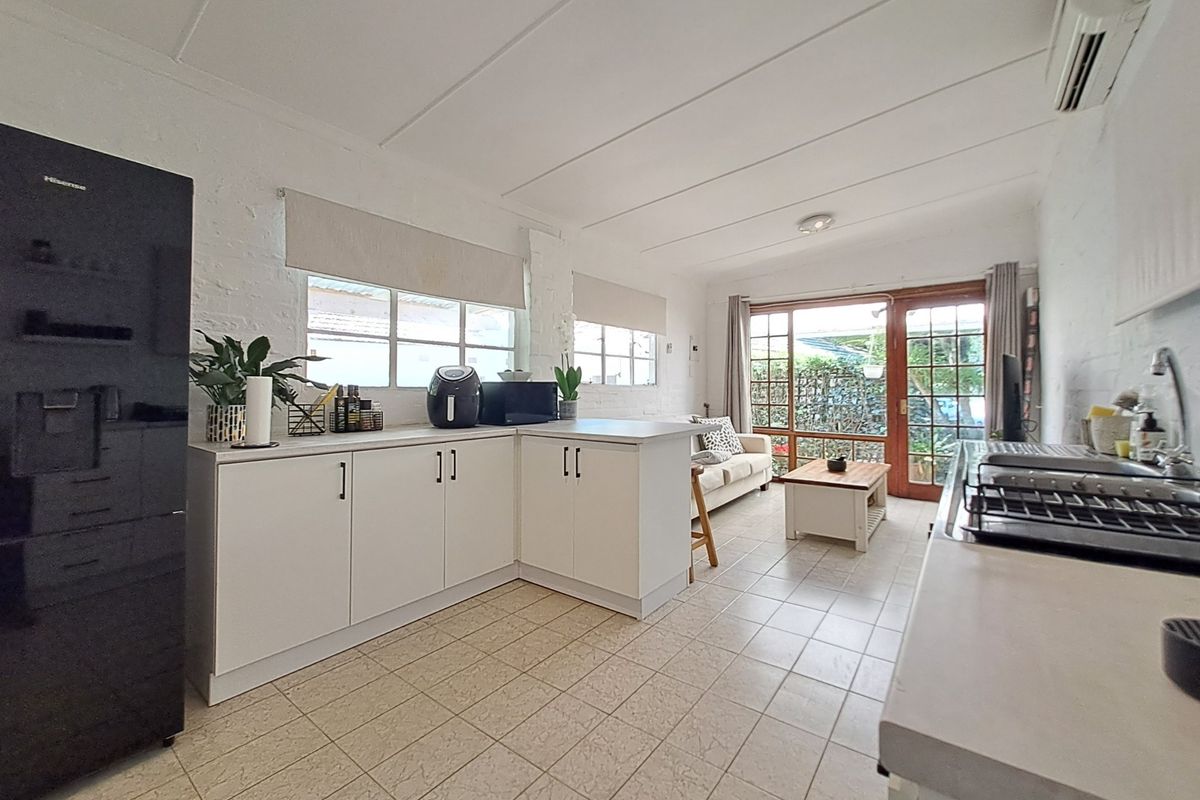 Open-plan kitchen and living area featuring tiled floors, white cabinetry, exposed brick walls, and direct access to the outdoor space through glass doors.