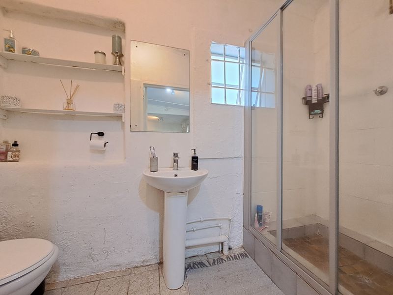 A compact bathroom featuring a pedestal basin, shower enclosure, and built-in wall shelving, with a rustic textured wall finish.