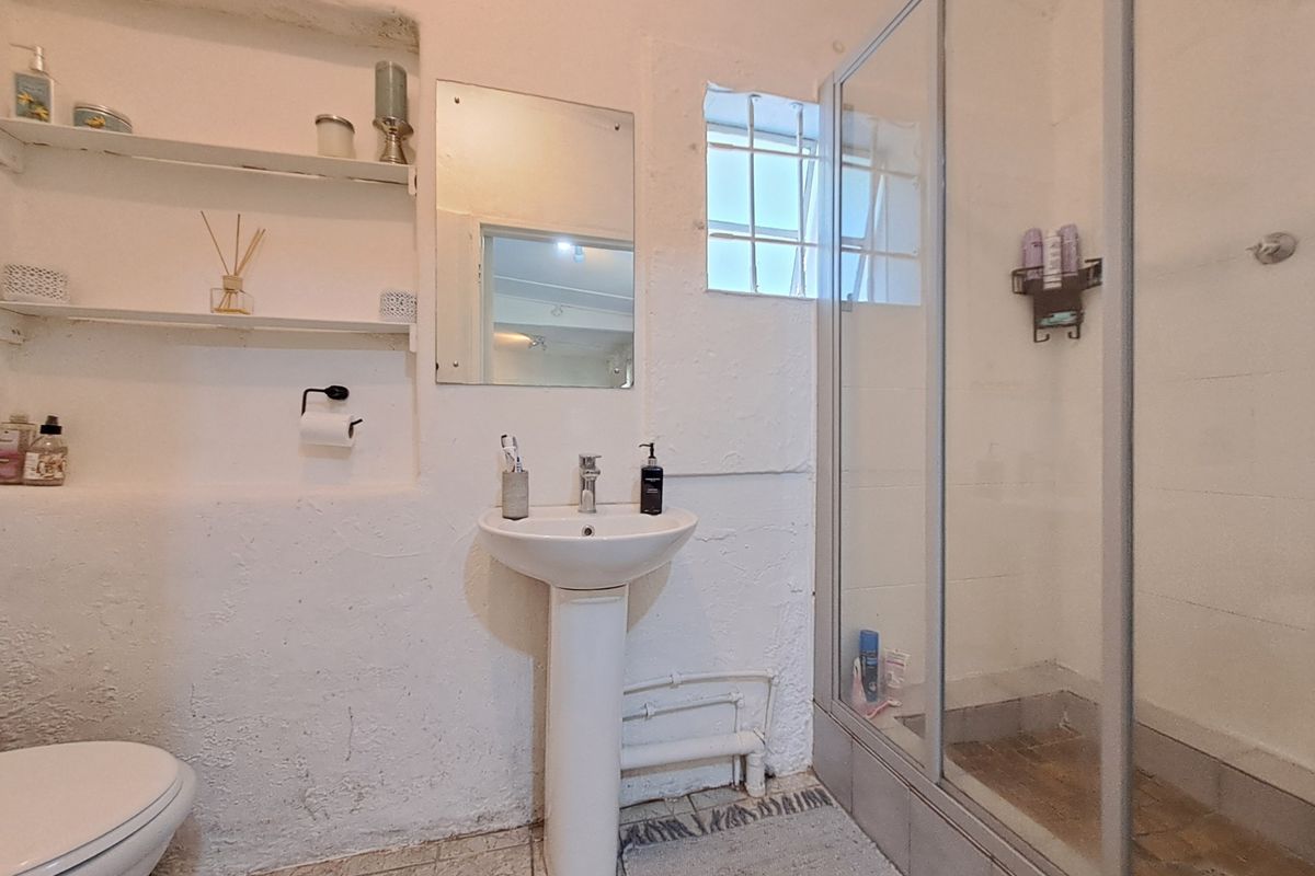 A compact bathroom featuring a pedestal basin, shower enclosure, and built-in wall shelving, with a rustic textured wall finish.