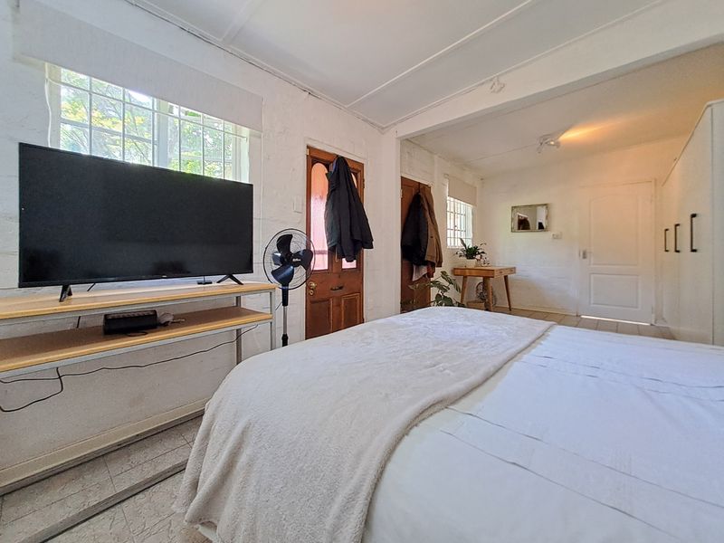 A bedroom featuring tiled flooring, exposed brick walls, and a timber door, offering a rustic cottage aesthetic with natural light.