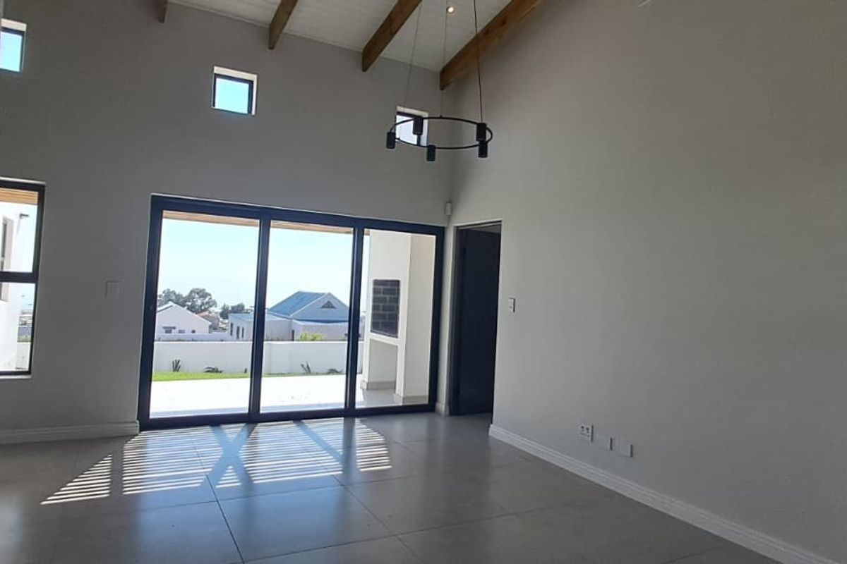 Spacious living area featuring high ceilings with exposed timber beams, large sliding glass doors leading to a patio, and modern tiled flooring.