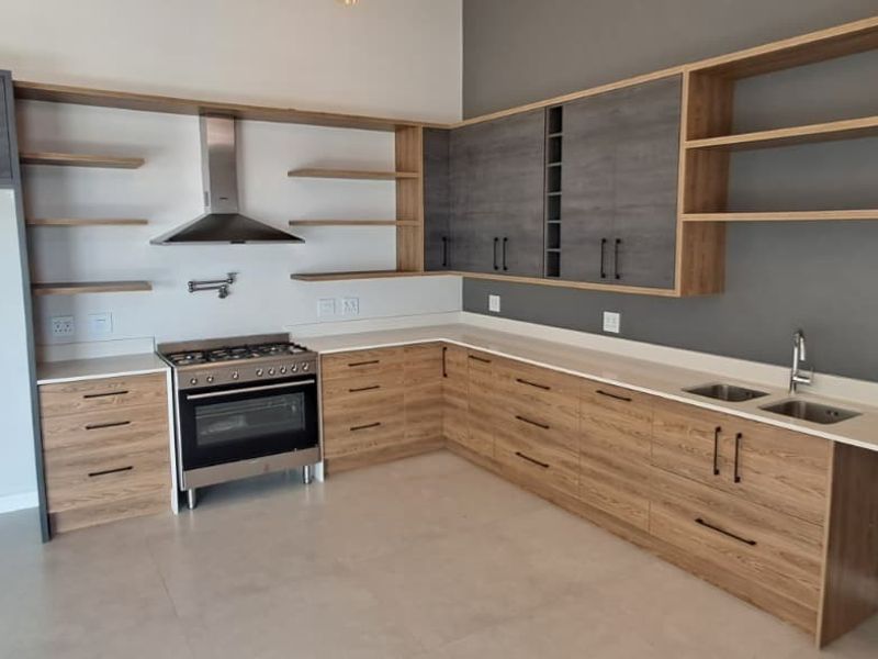 Modern kitchen featuring wood-grain and grey cabinetry, stone countertops, open shelving, and a stainless steel gas stove with extractor fan.