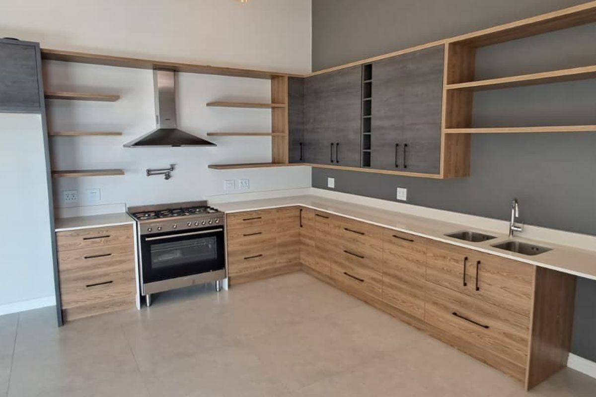 Modern kitchen featuring wood-grain and grey cabinetry, stone countertops, open shelving, and a stainless steel gas stove with extractor fan.