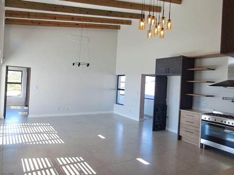 Spacious open-plan living and kitchen area featuring high ceilings with exposed timber beams, modern cabinetry, and a gas stove.