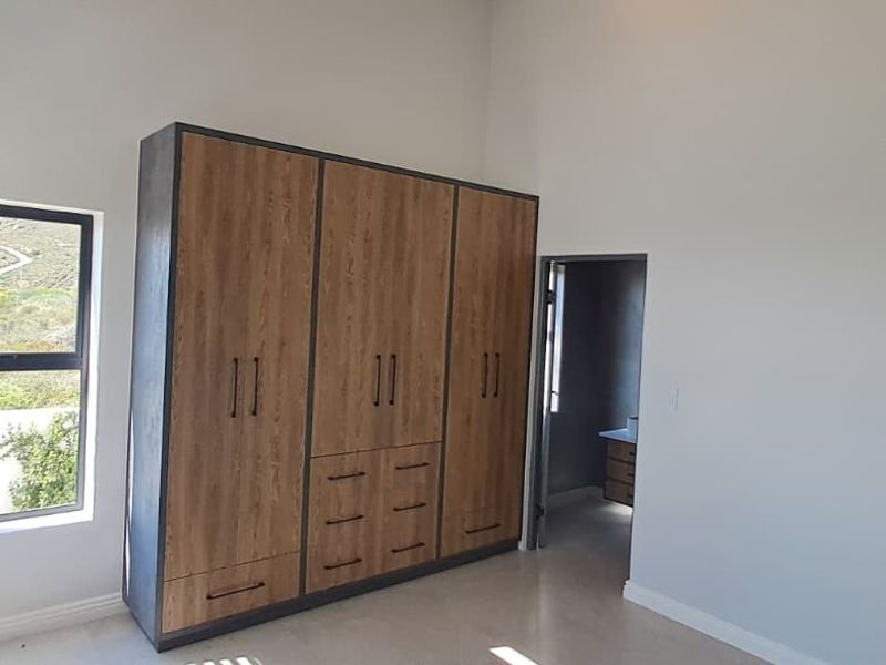 A bright, modern bedroom featuring high ceilings, neutral tiled flooring, and extensive built-in wooden cabinetry with integrated storage.