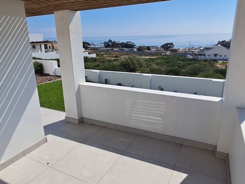 A modern covered patio featuring tiled flooring, a slatted timber ceiling, and a masonry balustrade, offering scenic coastal views.