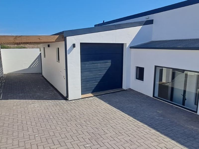 Modern exterior view featuring a paved driveway, garage access, timber pergola, and stone-clad architectural detailing.