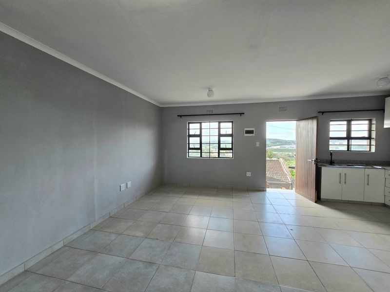 An open-plan living and kitchen area featuring neutral tiled flooring, grey walls, and built-in kitchen cabinetry with direct access to an outdoor space.