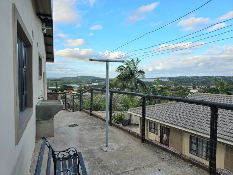 An elevated outdoor balcony featuring a concrete floor, utility sink, and metal railing, offering expansive views of the surrounding neighborhood.