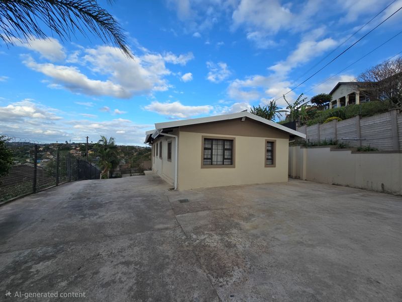 Exterior view of the property featuring a large concrete driveway, security fencing, and a retaining wall against a sloped landscape.