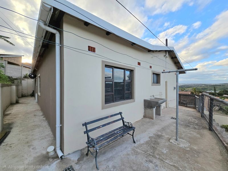 Rear exterior view of the apartment featuring a concrete patio area, a fixed outdoor wash basin, and aluminium window frames.