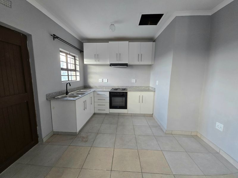A functional kitchen featuring white cabinetry, granite countertops, built-in oven and hob, and tiled flooring in an open-plan layout.