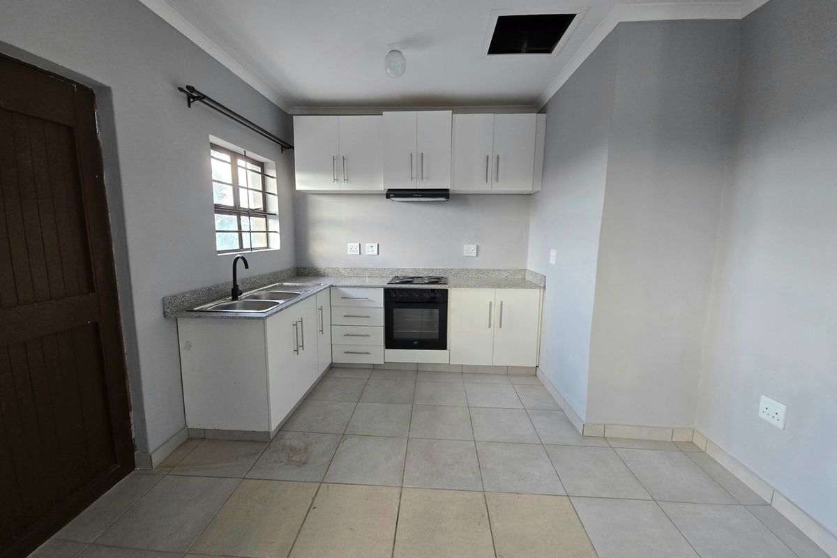 A functional kitchen featuring white cabinetry, granite countertops, built-in oven and hob, and tiled flooring in an open-plan layout.