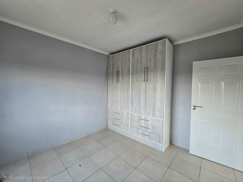 A clean, empty bedroom featuring neutral grey walls, tiled flooring, and a modern built-in wardrobe with ample storage space.