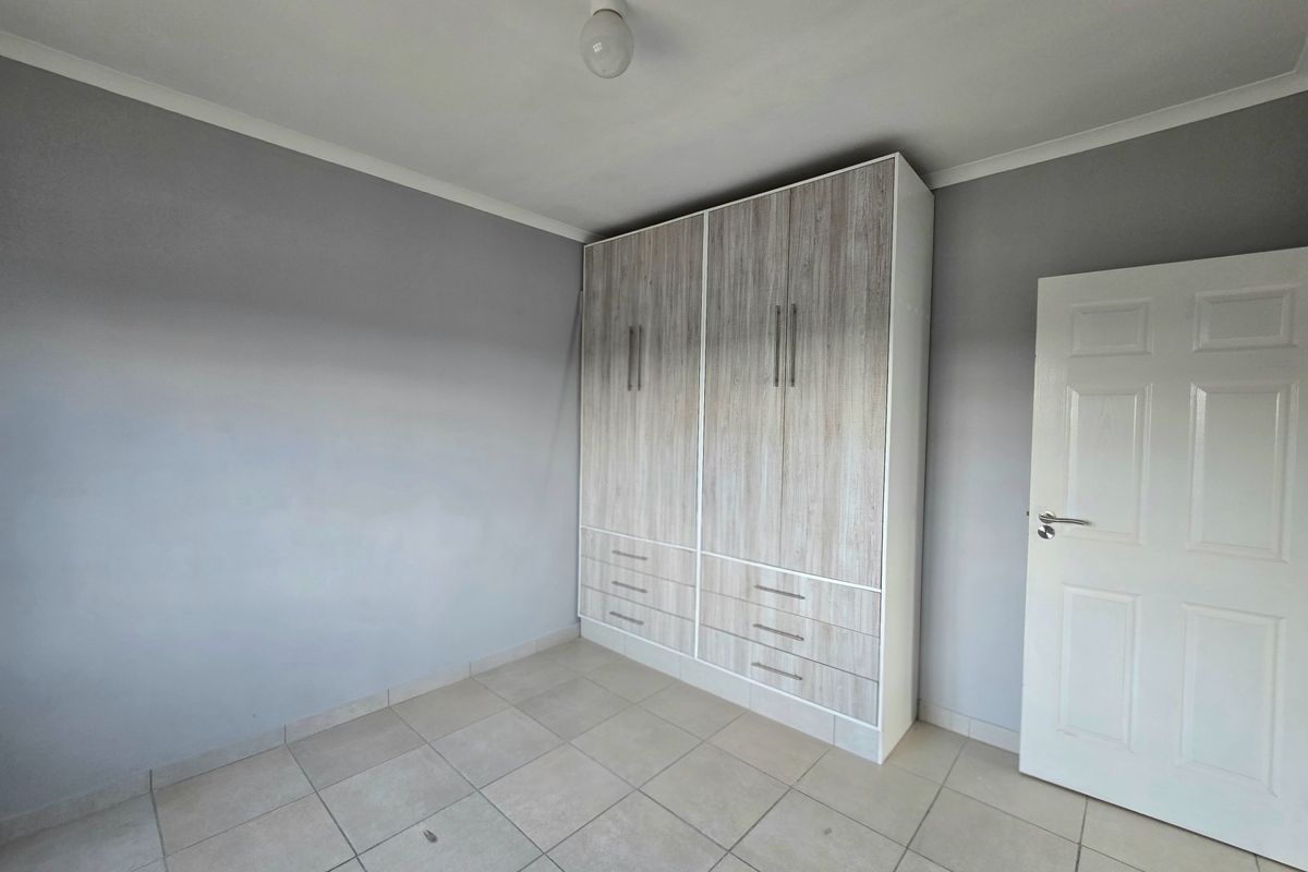 A clean, empty bedroom featuring neutral grey walls, tiled flooring, and a modern built-in wardrobe with ample storage space.