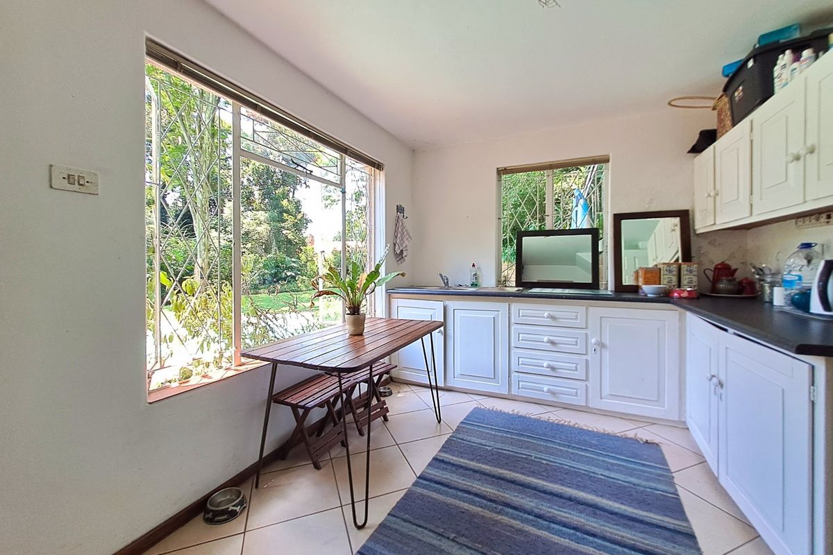 A functional kitchen featuring white built-in cabinetry, dark countertops, and large windows with security bars, overlooking the garden area.