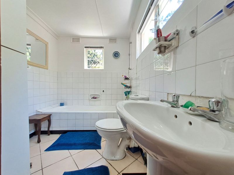 A functional bathroom featuring a bathtub, pedestal basin, and toilet with white wall tiling and neutral floor tiles.