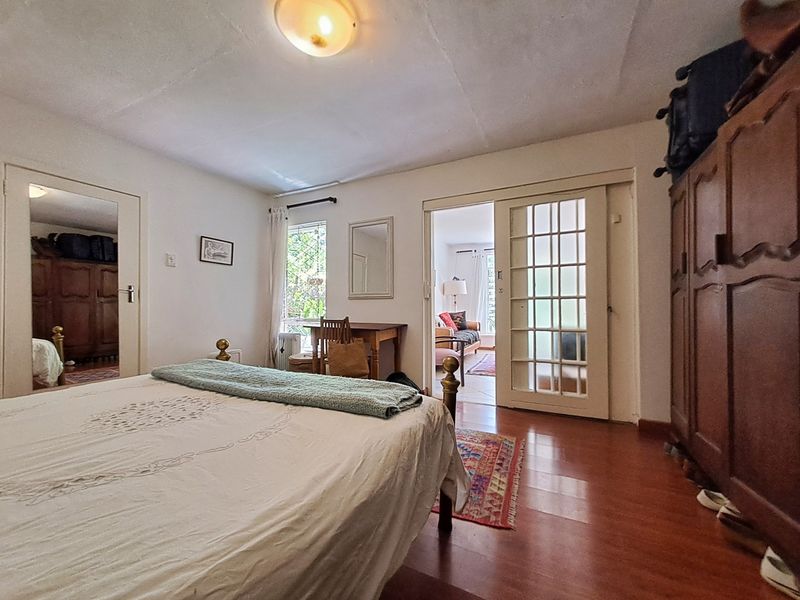 A bedroom featuring laminate flooring, a sliding glass panel door leading to an adjacent room, and a window providing natural light.
