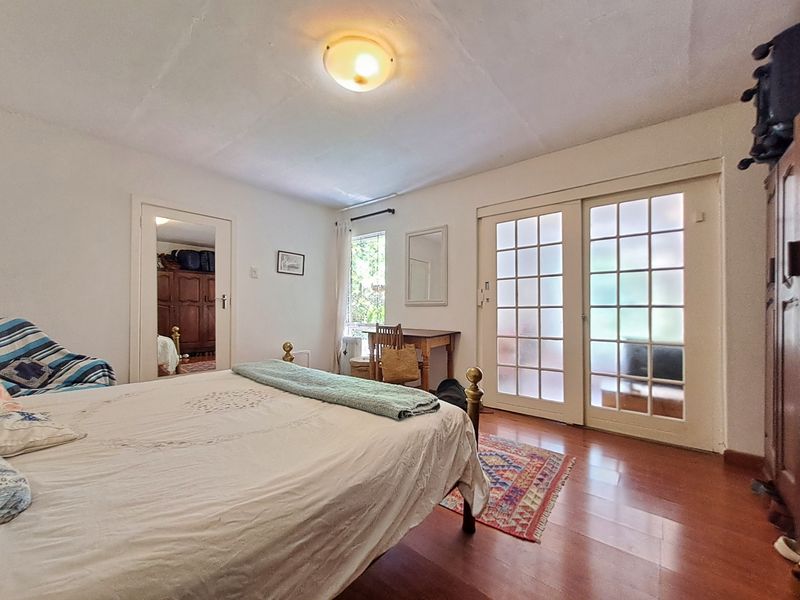 A bedroom featuring laminate flooring, a built-in mirror door, and glass-paneled french doors providing natural light and access to the exterior.