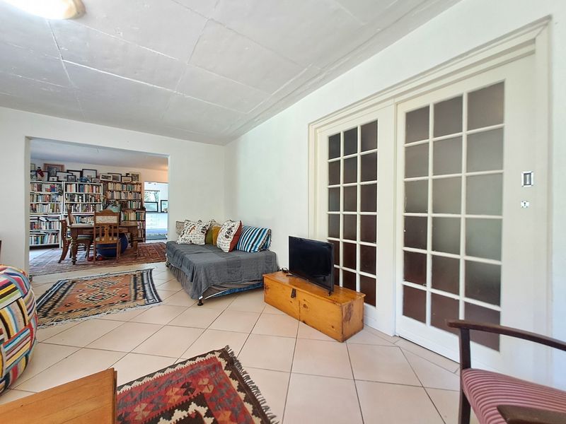 Open plan living area featuring tiled flooring and classic French doors, leading into an adjacent dining space with built-in shelving.