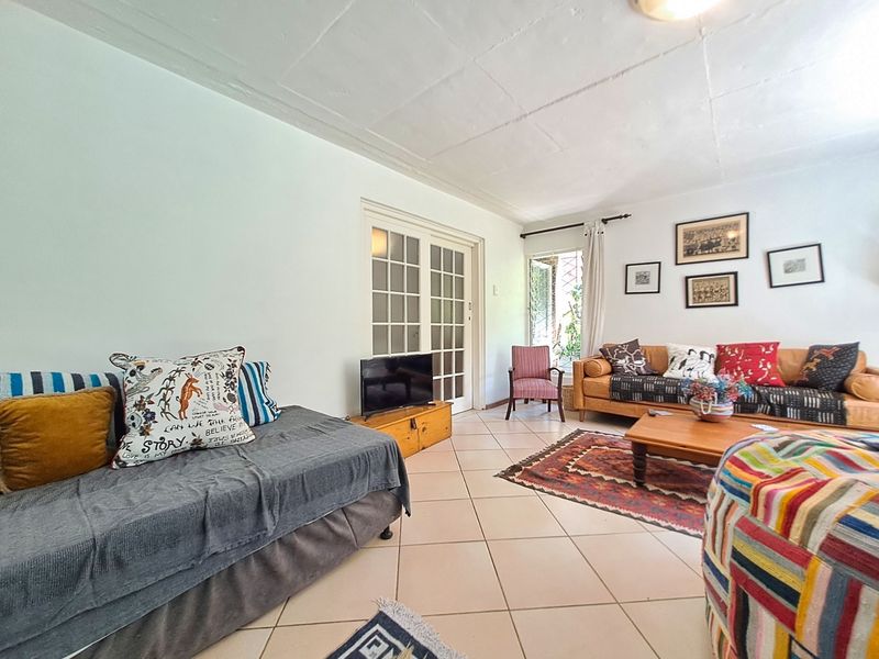 A spacious living room featuring tiled flooring, exposed beam ceiling, and classic french doors leading to the exterior.