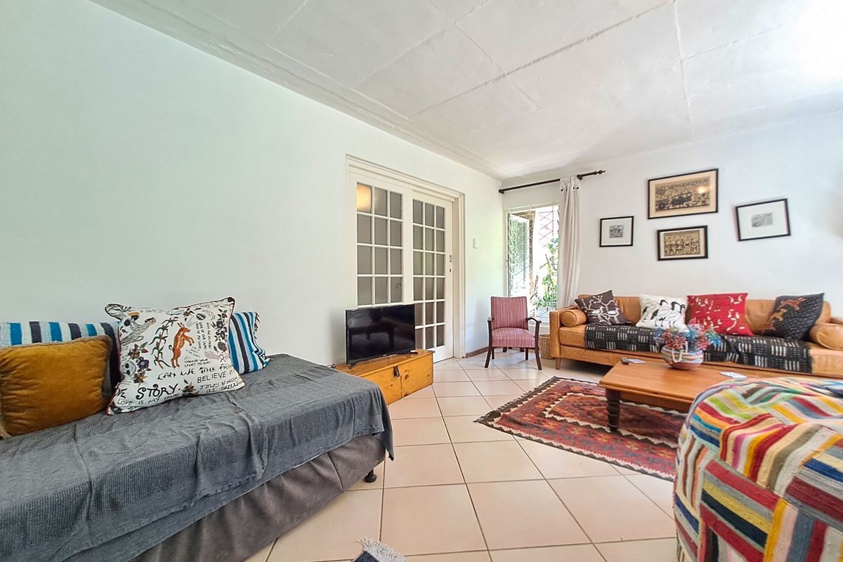 A spacious living room featuring tiled flooring, exposed beam ceiling, and classic french doors leading to the exterior.