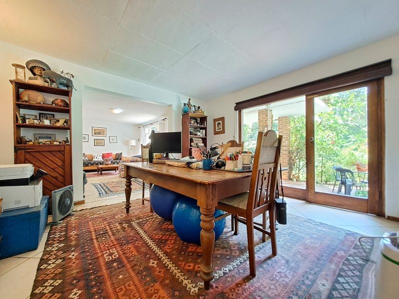 A bright living area featuring tiled flooring, exposed beam ceilings, and large sliding glass doors providing direct access to the garden patio.